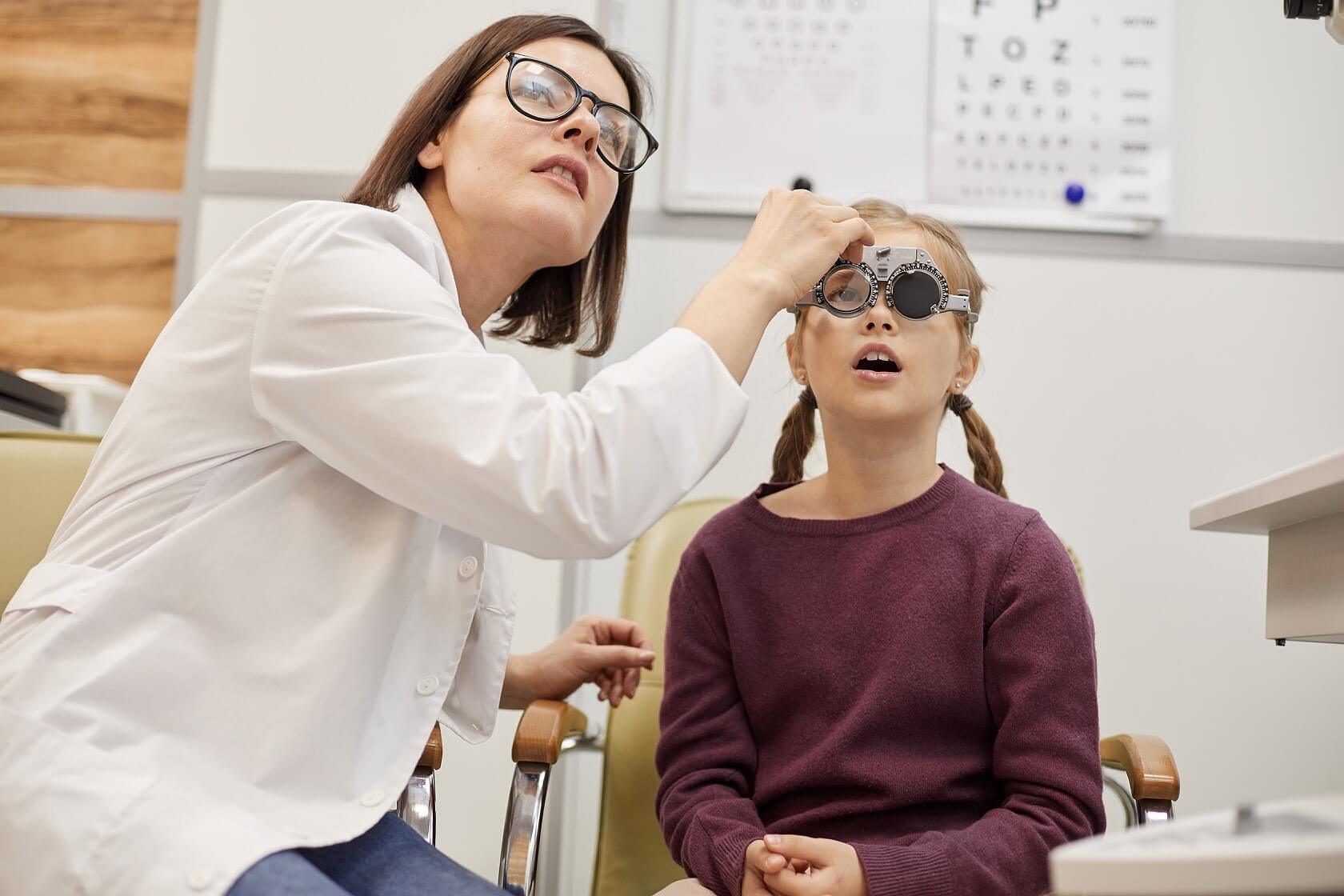 Eye Doctor using a trail frame to measure the power of the eyes on a girl